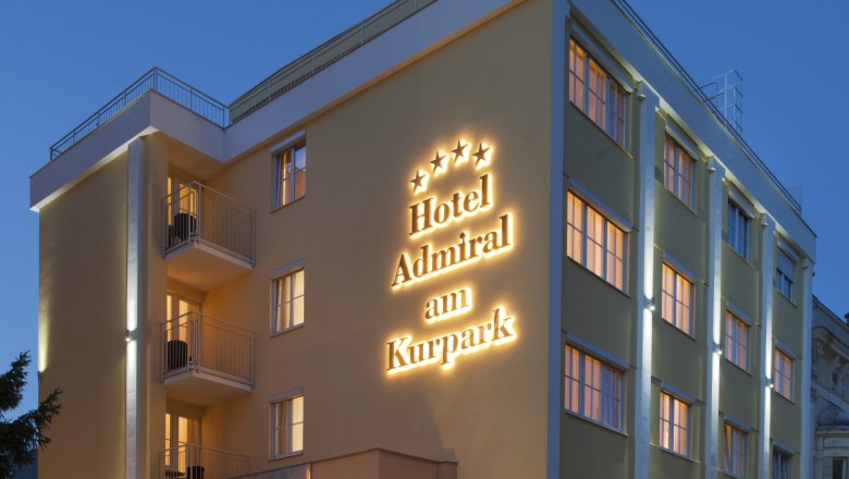 Außenansicht, © Hotel Admiral Außenansicht eines Hotels bei Dämmerung mit beleuchtetem Schriftzug "Hotel Admiral am Kurpark".