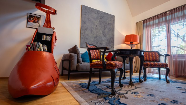 Ein stilvoll eingerichtetes Hotelzimmer mit einem großen roten Schuh als Bücherregal, antiken Stühlen, einem Tisch und einer Stehlampe.