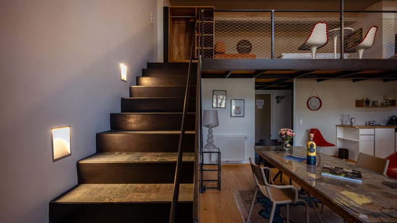 Innenansicht eines modernen Hotelzimmers mit Treppe, Tisch und Stühlen.