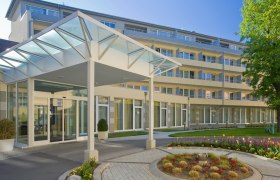 Moderner Geb&auml;udeeingang mit Glasdach und Garten.