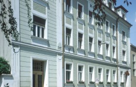 Exterior view of a multi-storey building with a green façade and white window frames.