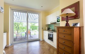 Helle Küche mit Parkettboden, Schrank, Herd und großer Glastür zur Terrasse mit Markise.