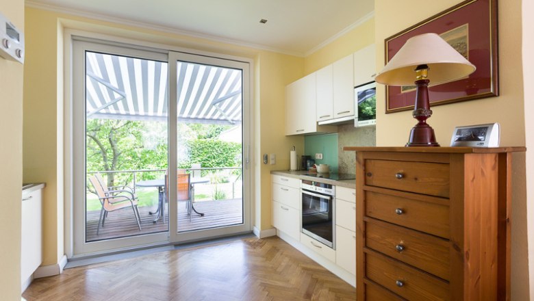 Helle Küche mit Parkettboden, Schrank, Herd und großer Glastür zur Terrasse mit Markise.