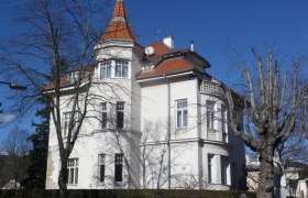 Large white house with a red roof and tower, surrounded by bare trees.