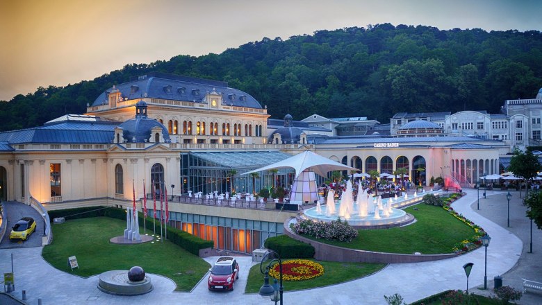 Au&szlig;enansicht des Congress Centers Baden mit beleuchtetem Springbrunnen und umliegender Natur.