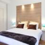 Modern bedroom with double bed, wooden back wall and blue bedside lamps.