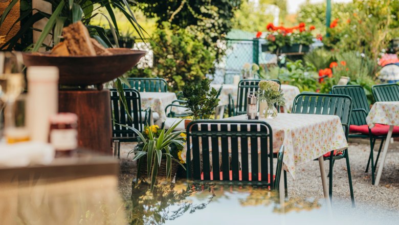 A cozy guest garden with tables and chairs, surrounded by plants and flowers.