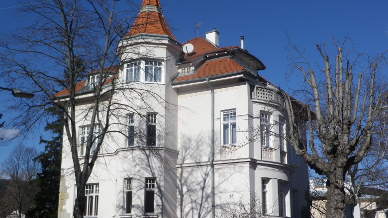 Large white house with a red roof and tower, surrounded by bare trees.