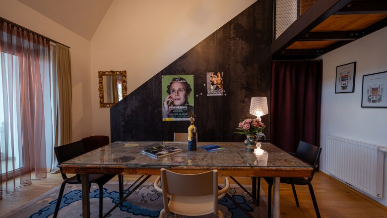 Ein stilvoll eingerichteter Raum mit einem Tisch, Stühlen, einer Lampe und Postern an der Wand.